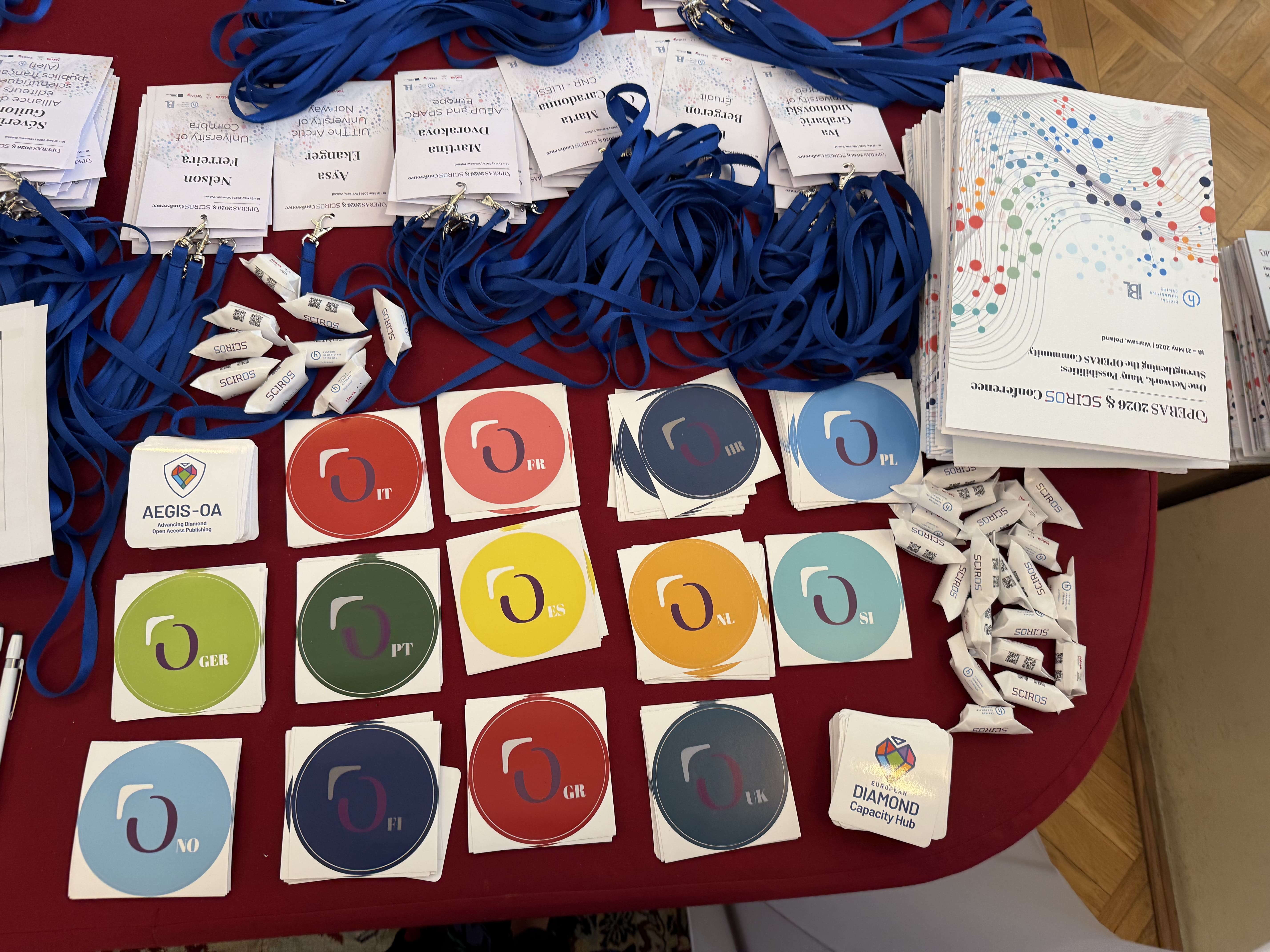 Photo of the OPERAS 2026 registration desk featuring OPERAS National Nodes stickers, EDCH and AEGIS-OA stickers.